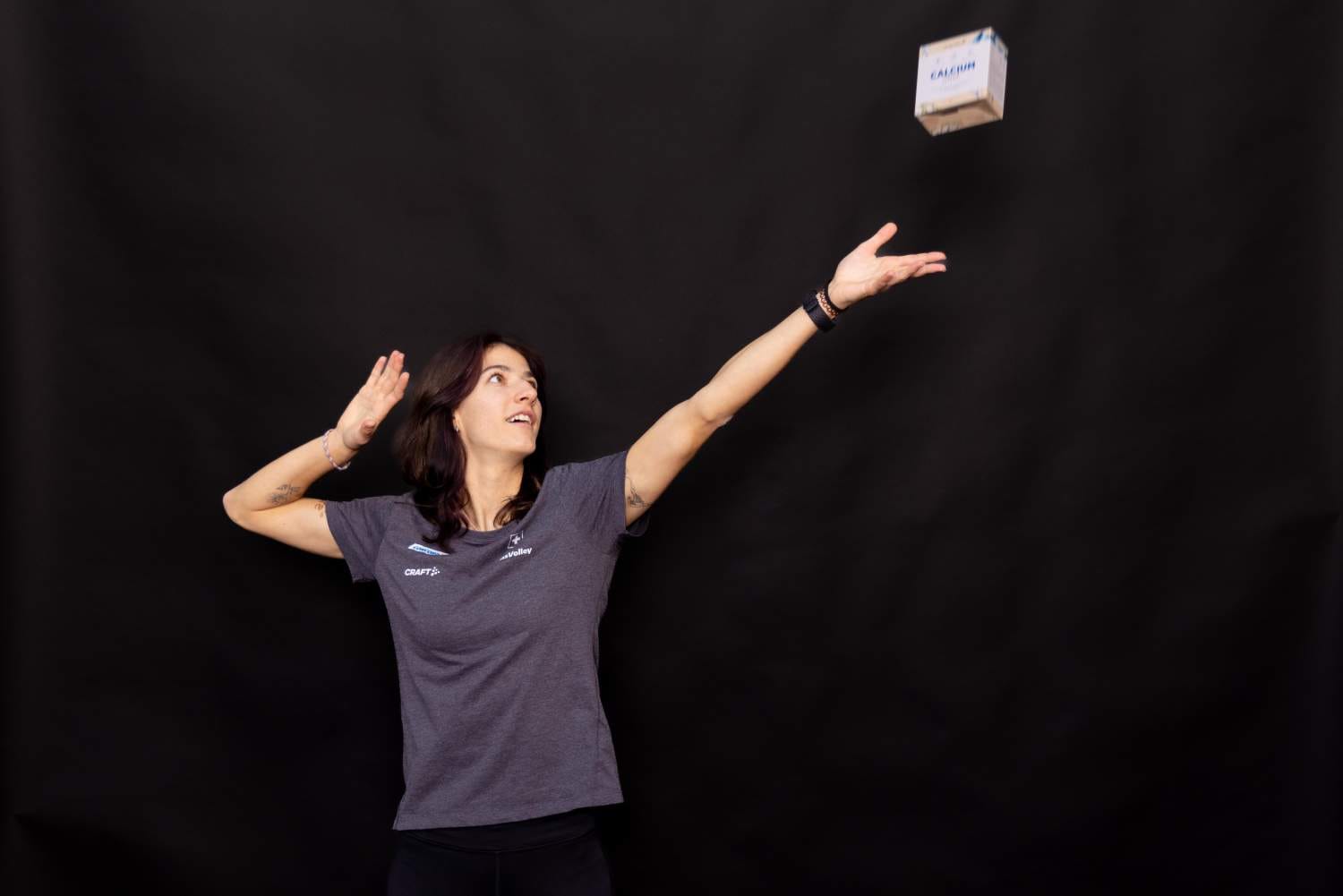 Janick Schaltegger fängt eine Frau in einem grauen Hemd vor einem schwarzen Hintergrund ein, die einen Arm nach oben streckt, während sie eine kleine Schachtel mit der Aufschrift LASHIN in die Luft wirft.