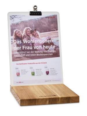 Ein Flyer auf einem Klemmbrett der Verkaufssteller Theke zeigt drei lächelnde Frauen an einem See, die auf Deutsch Informationen über das Wohlbefinden von Frauen und Schweizer Nahrungsergänzungsmittel geben. Am unteren Rand des Flyers sind vier Nahrungsergänzungsmittel abgebildet.