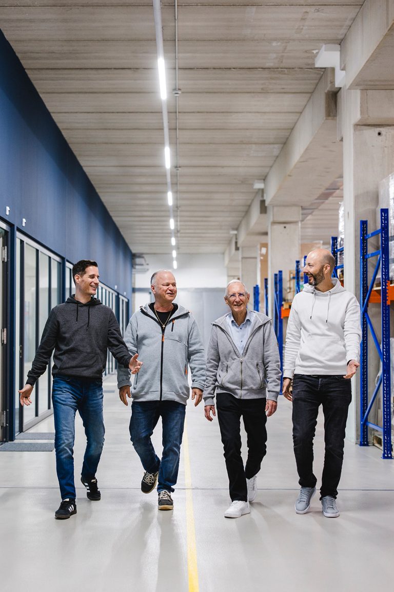 Vier Männer, darunter Mitglieder des kingnature-Verwaltungsrats, gehen gemeinsam lächelnd und unterhaltend einen hell erleuchteten Industrieflur entlang, inmitten von freiliegenden Betondecken und Wandregalen.