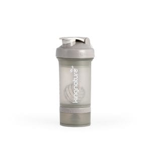Ein durchscheinend grauer Shaker „Blender Bottle ProStak Pro“ mit Klappdeckel, Metall-Mixkugel und kingnature-Logo an der Seite. Im Boden befindet sich ein abnehmbares Aufbewahrungsfach mit der Aufschrift „ProStak“.